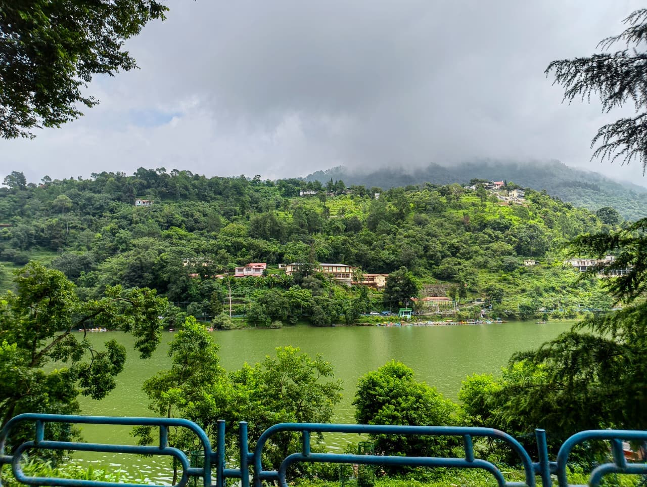 A green lake and forested hillside seen from a road above Bhimtal