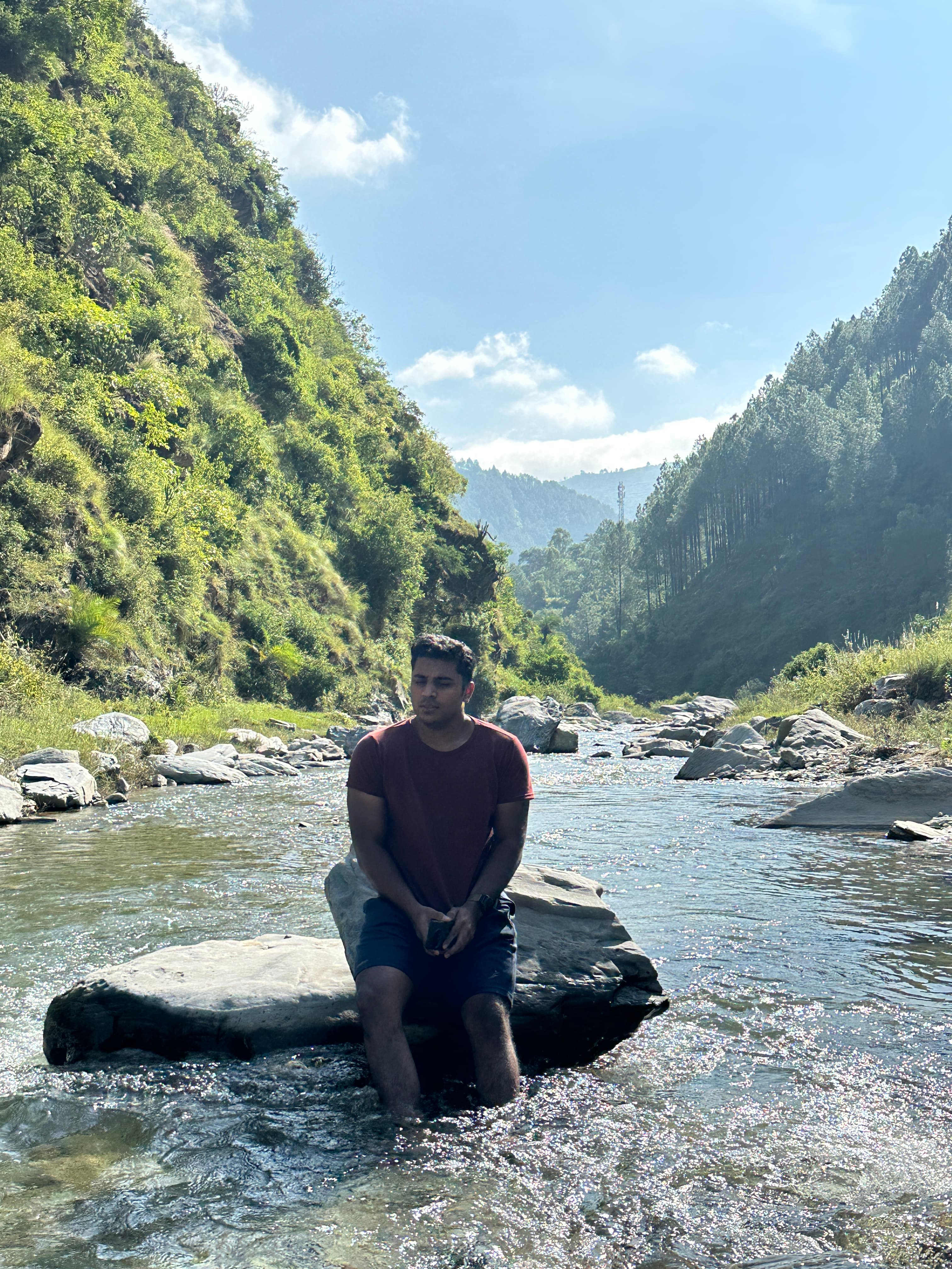 Sarthak sitting on a rock in the clear mountain stream near Blue Lotus