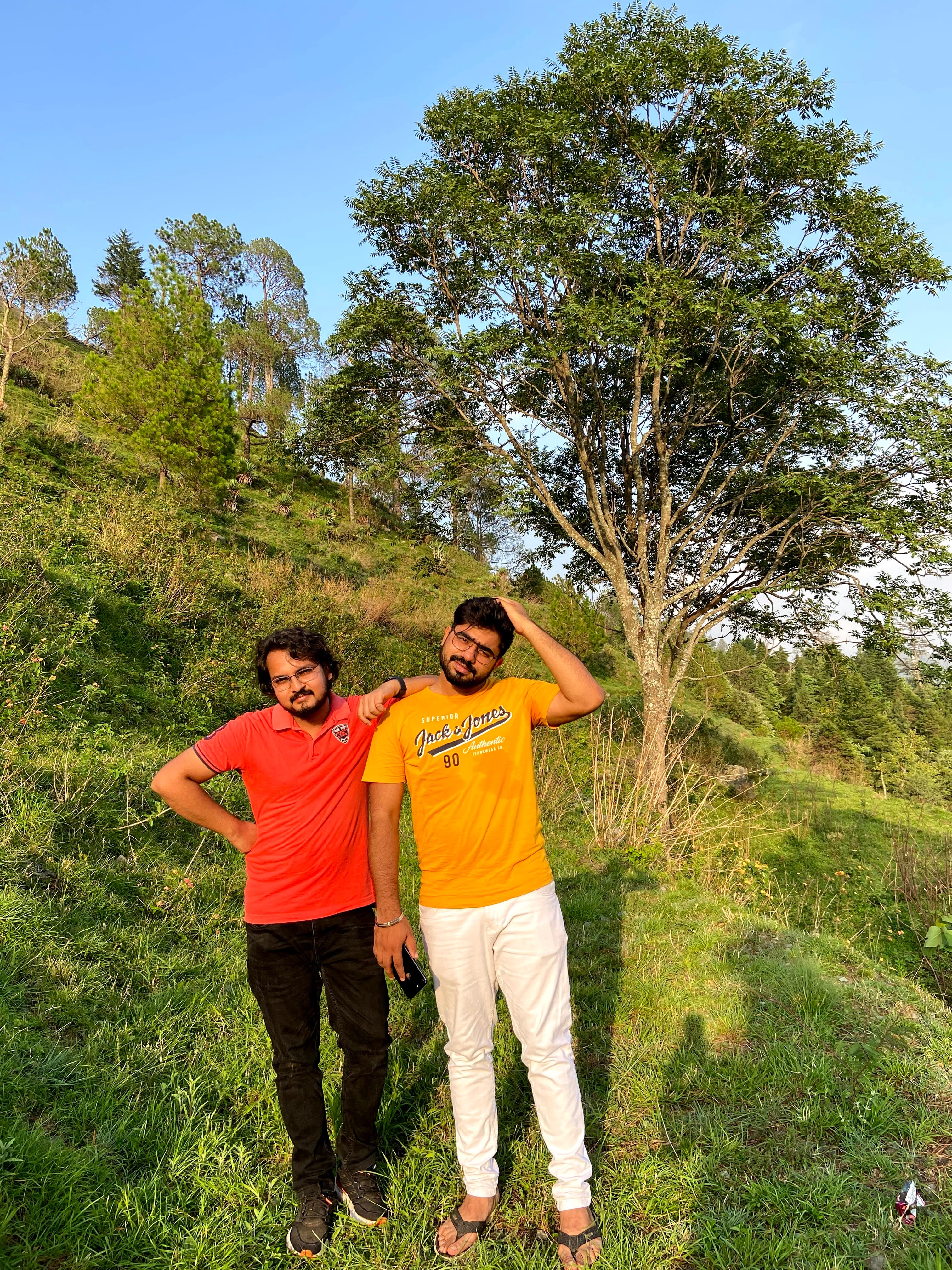 Charu Joshi and a friend standing beneath a tree on a sunny hillside near Bhimtal