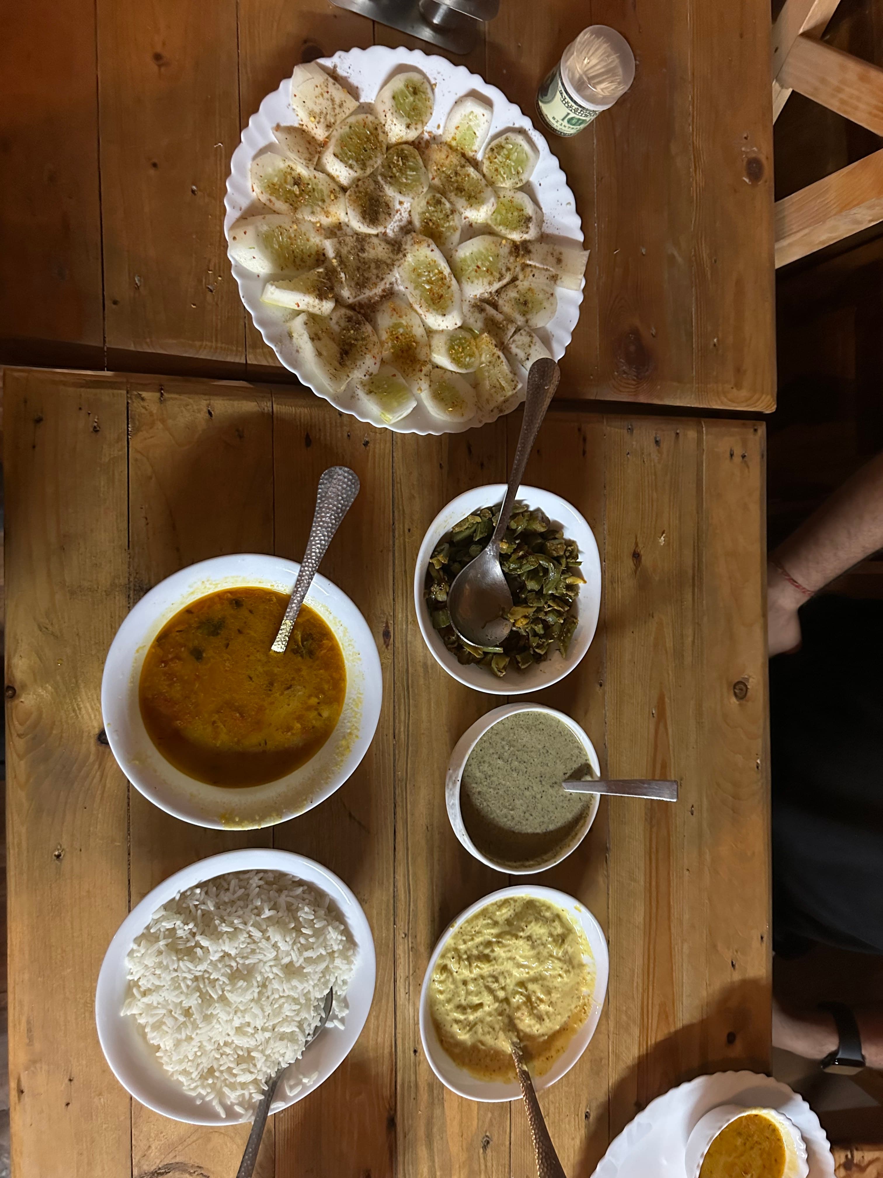 A Pahadi meal with rice, dal, vegetables, raita, cucumber, and local accompaniments on a wooden table