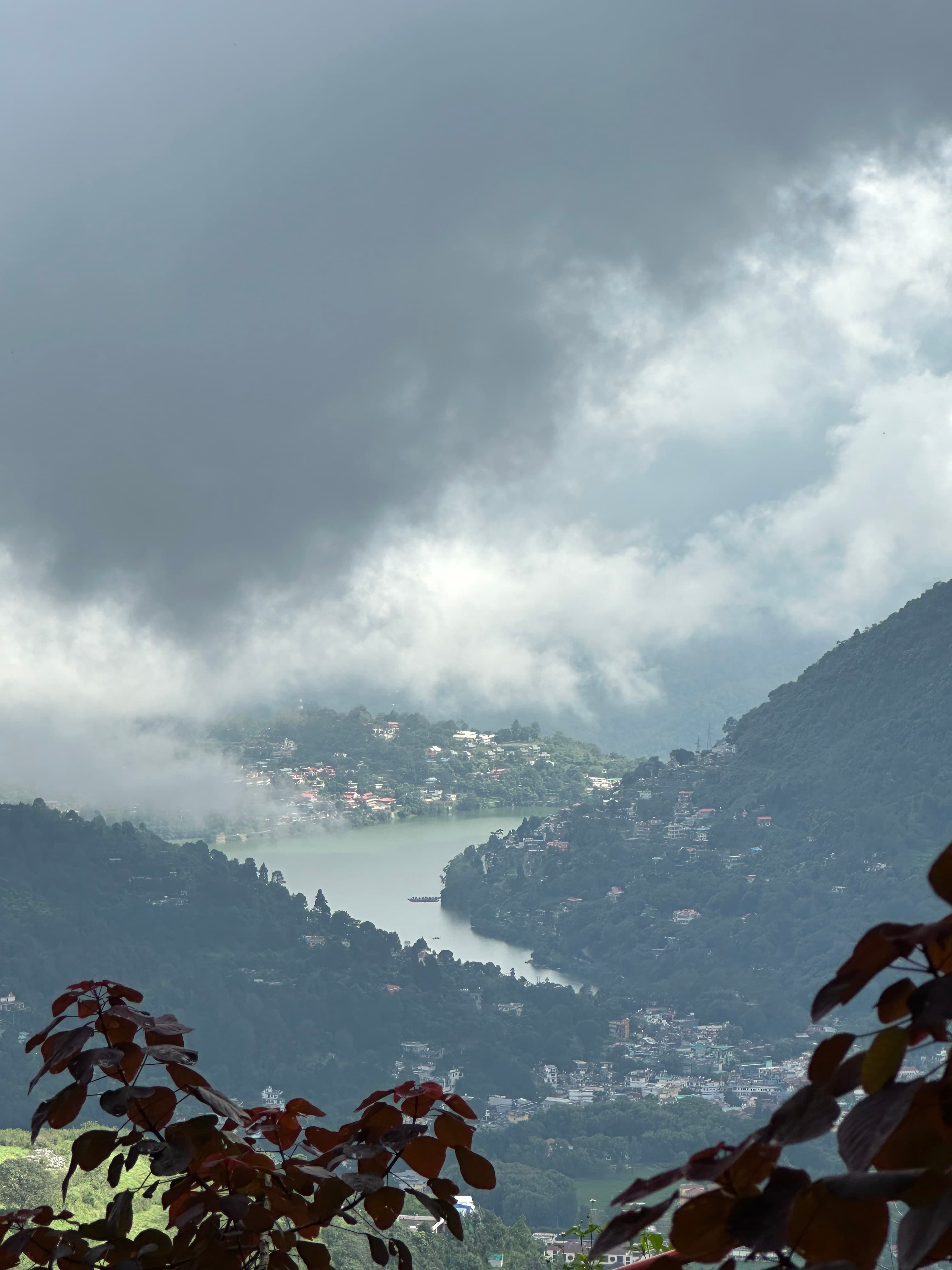 A mountain lake and hillside town appearing between low monsoon clouds