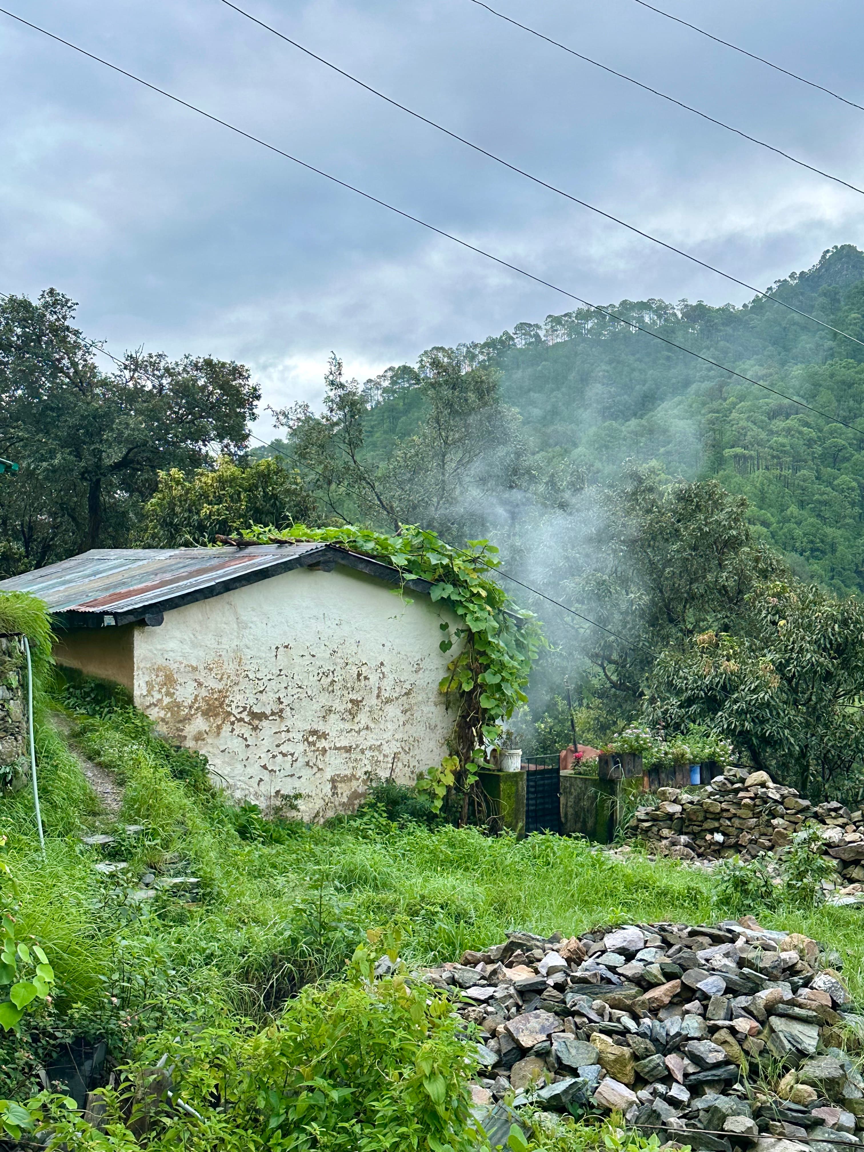 Smoke rising beside a small stone home in a green mountain settlement