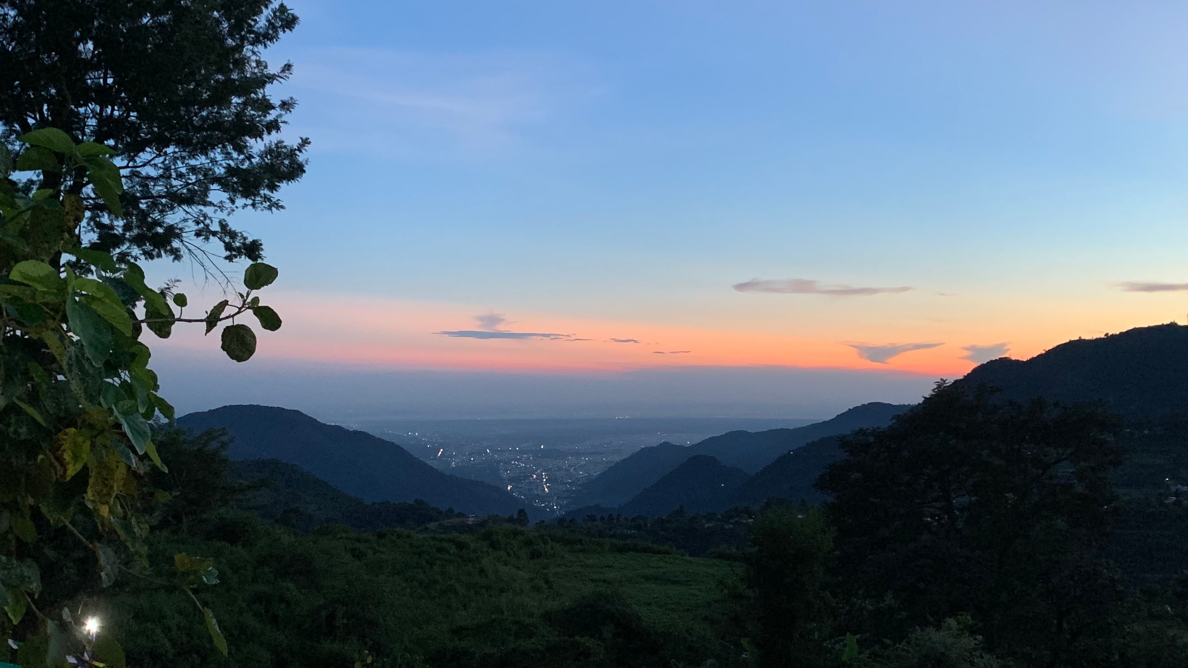The plains appearing beyond dark mountain ridges beneath an orange evening sky