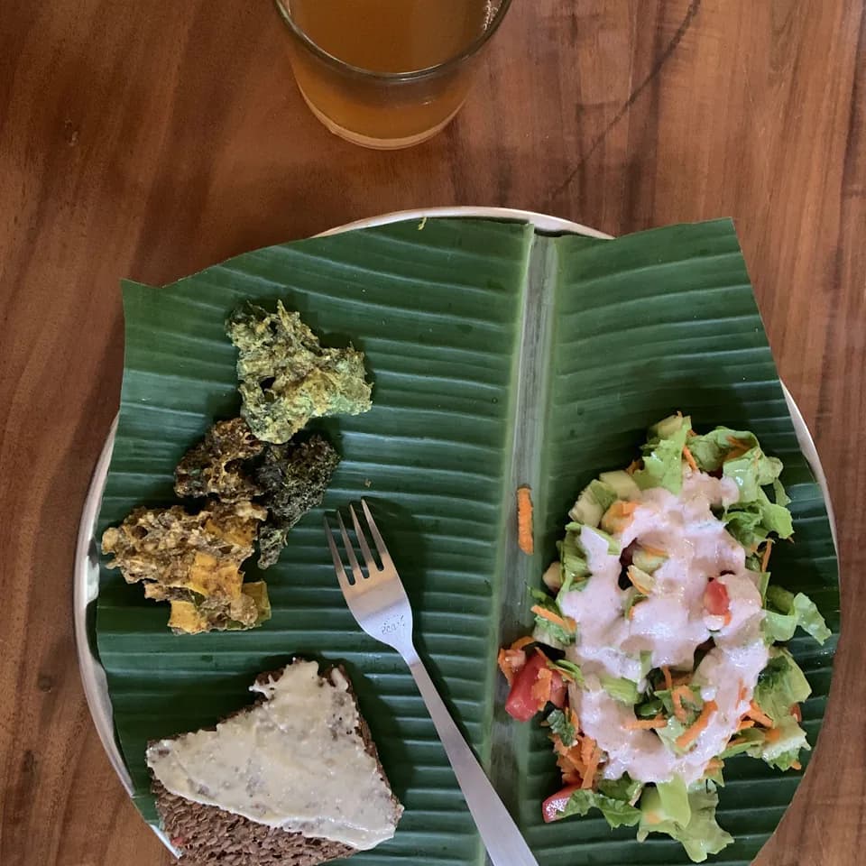 An uncooked meal served on a banana leaf with a glass of kombucha